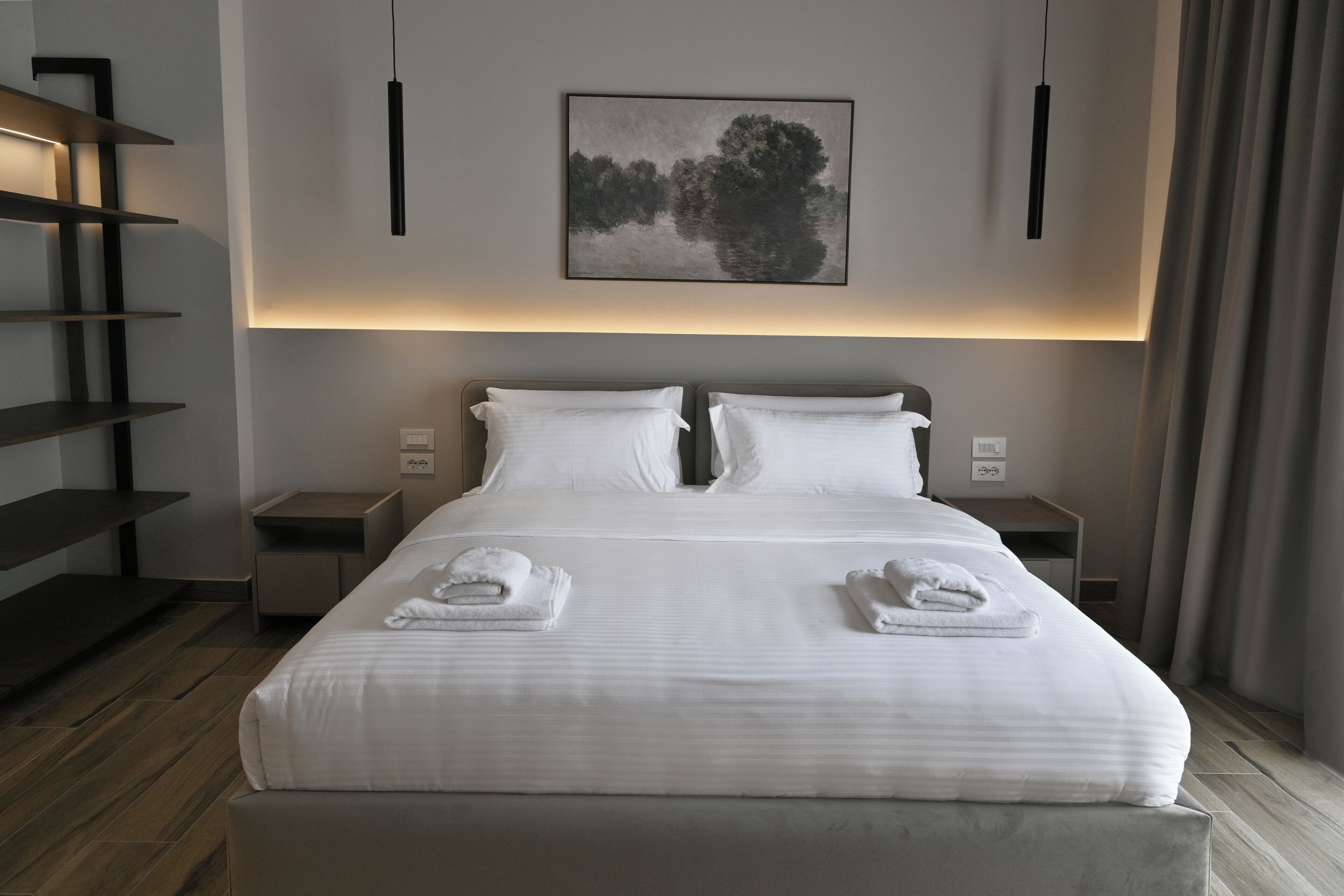 A modern hotel room with a large bed, two bedside tables, a wall-mounted artwork, and a wooden floor.