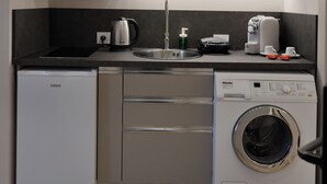 A compact kitchen with a dishwasher, washing machine, and a stainless steel range hood. - Cosmos Luxury Studio Suites (Tirana)