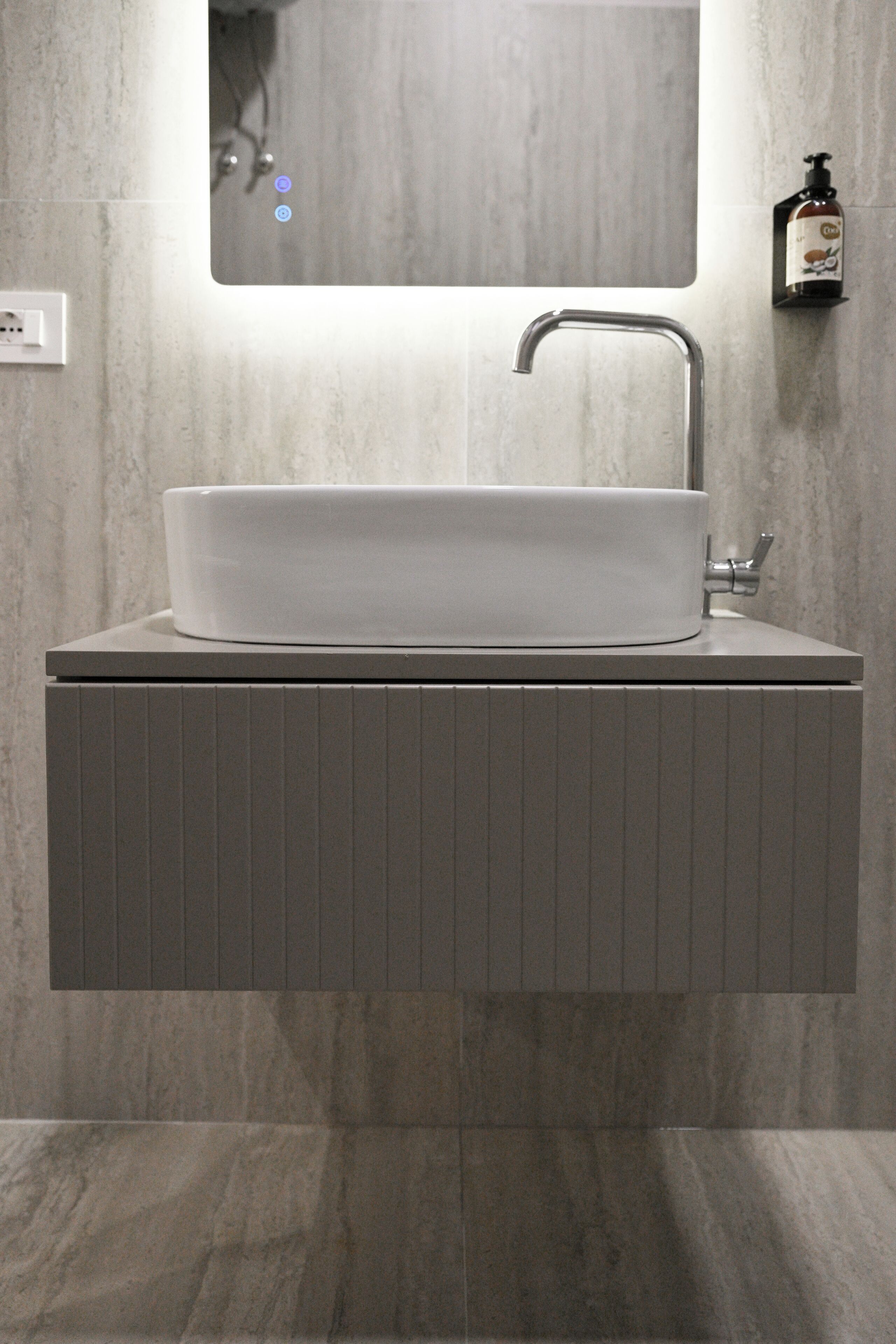 A bathroom with a white vessel sink, a mirror above it, and a soap dispenser on the wall.