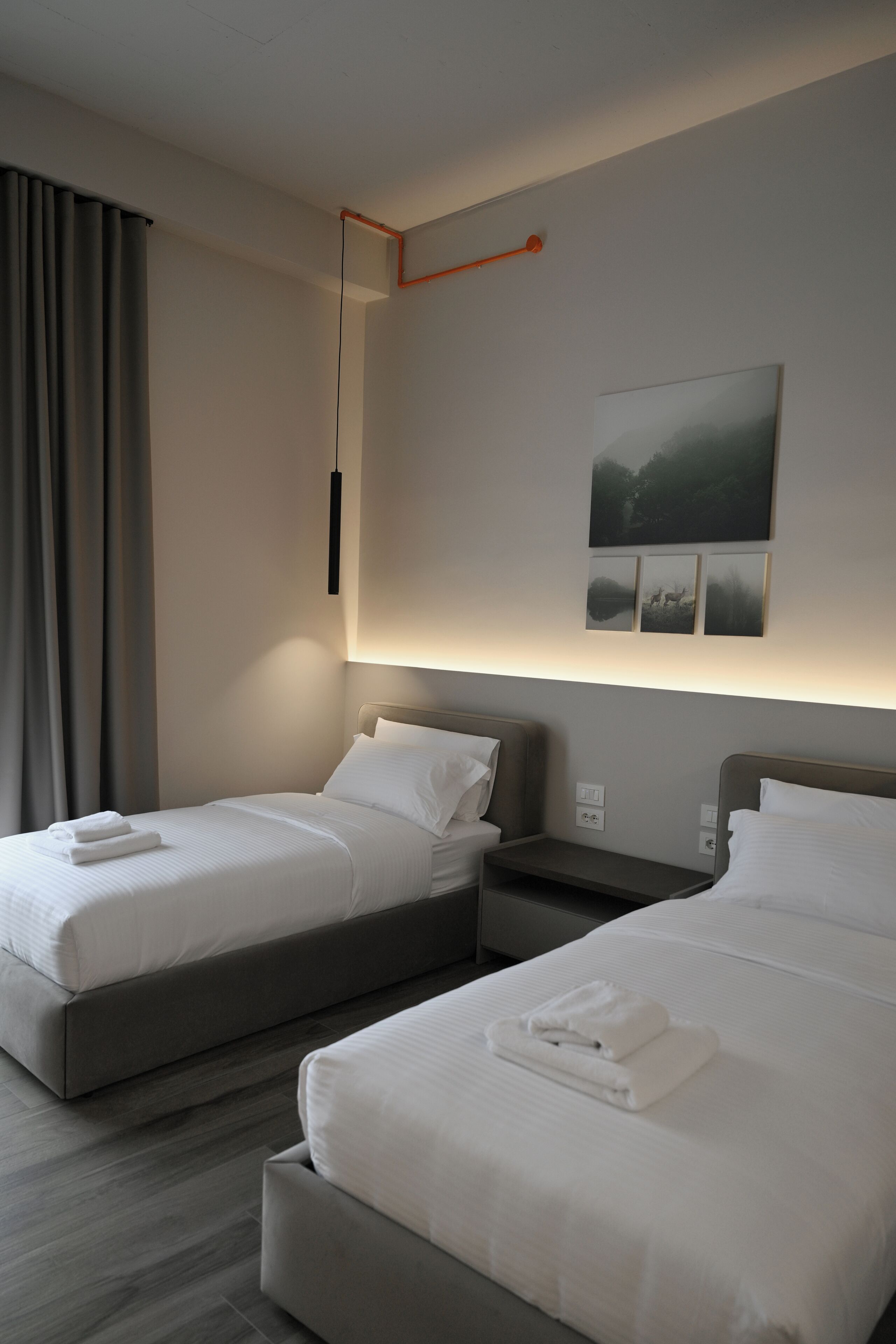 A hotel room with two beds, a bedside table, a wall-mounted light, and a painting.
