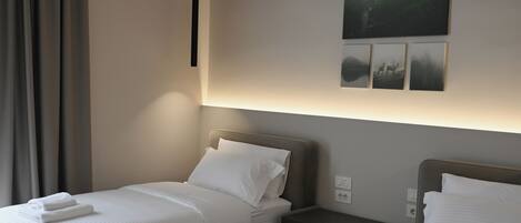 A hotel room with two beds, a bedside table, a wall-mounted light, and a painting.