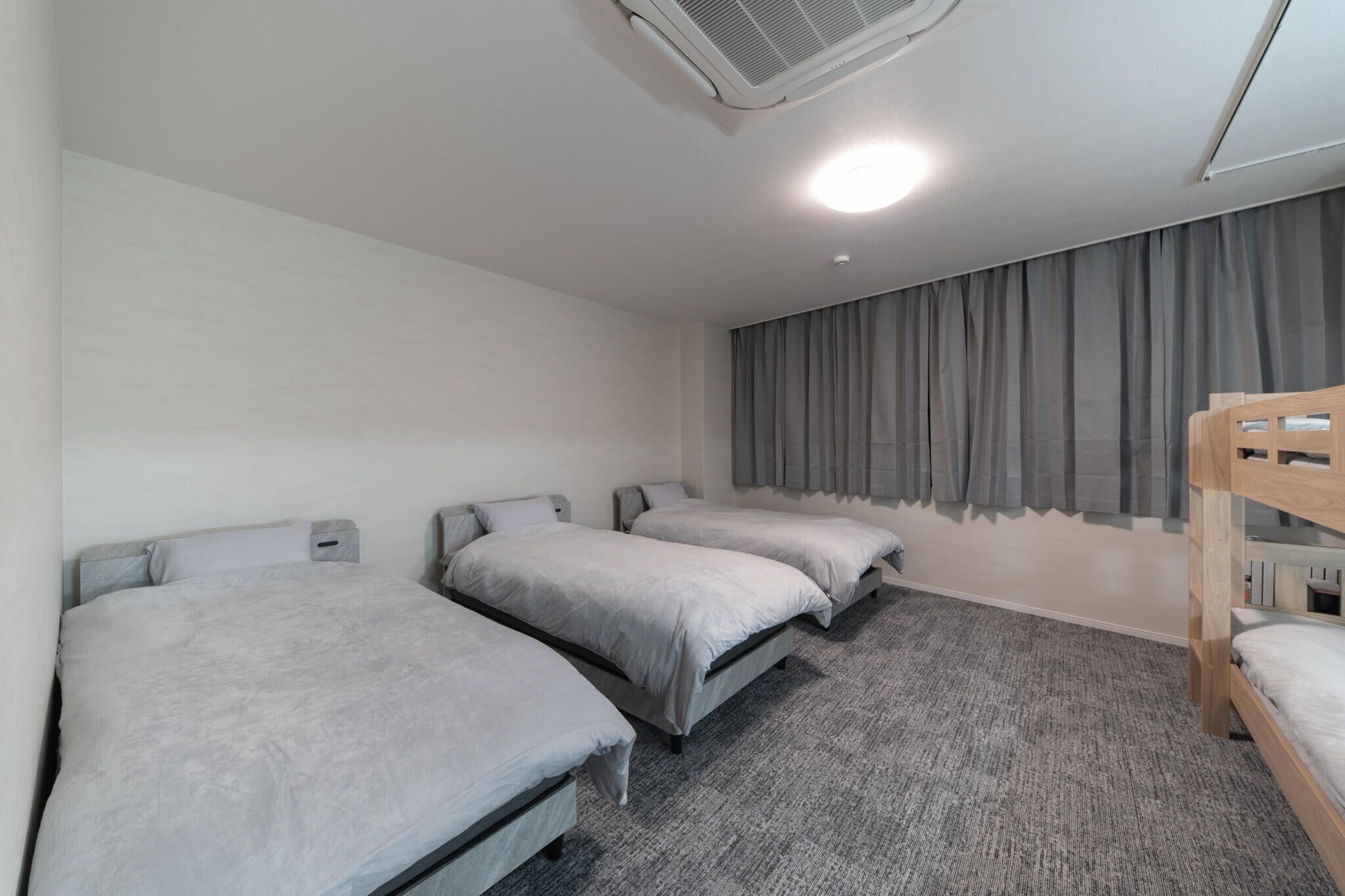 A room with three single beds, a bunk bed, a ceiling fan, and a window with curtains.
