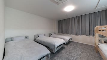 A room with three single beds, a bunk bed, a ceiling fan, and a window with curtains.
