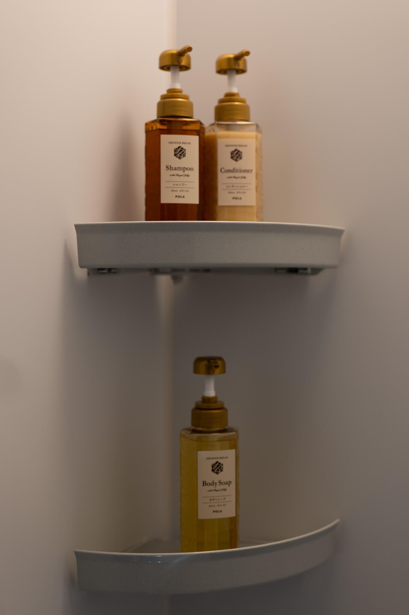 Una repisa en el baño con tres botellas de productos de cuidado personal: champú, acondicionador y jabón de baño.