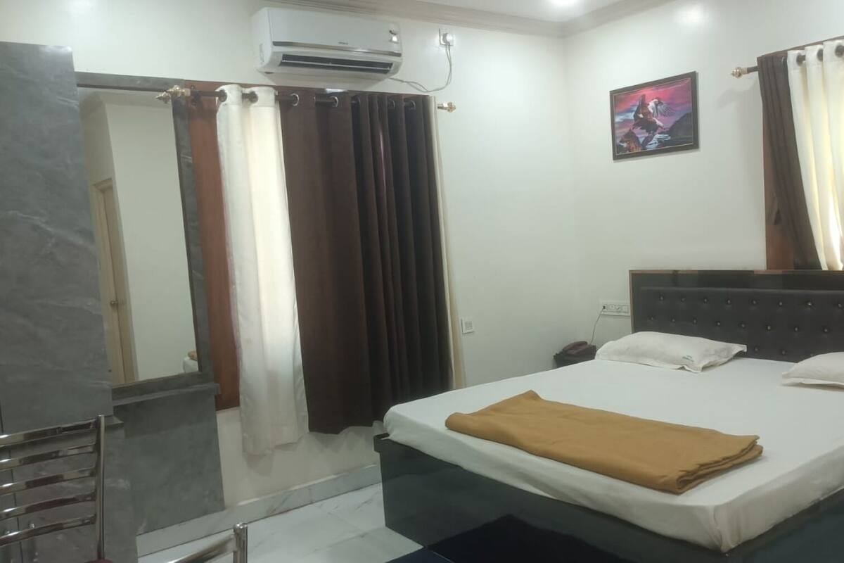 Habitación de hotel con cama, mesita de noche, espejo, equipo de aire acondicionado y un cuadro en la pared.