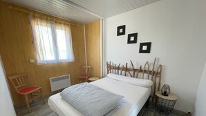 Ein Schlafzimmer mit Bett, Stuhl, Nachttisch und einem Fenster mit Vorhängen.