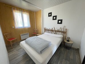 A bedroom with a bed, a chair, a small table, and a window with curtains. - Large-capacity chalet in Gruissan-plage (Gruissan)