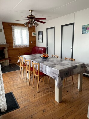 A dining area with a table, chairs, a ceiling fan, a fireplace, and a door. - Large-capacity chalet in Gruissan-plage (Gruissan)