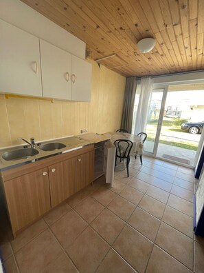 A kitchen with wooden cabinets, a countertop, and a dining area with a chair. - Large-capacity chalet in Gruissan-plage (Gruissan)