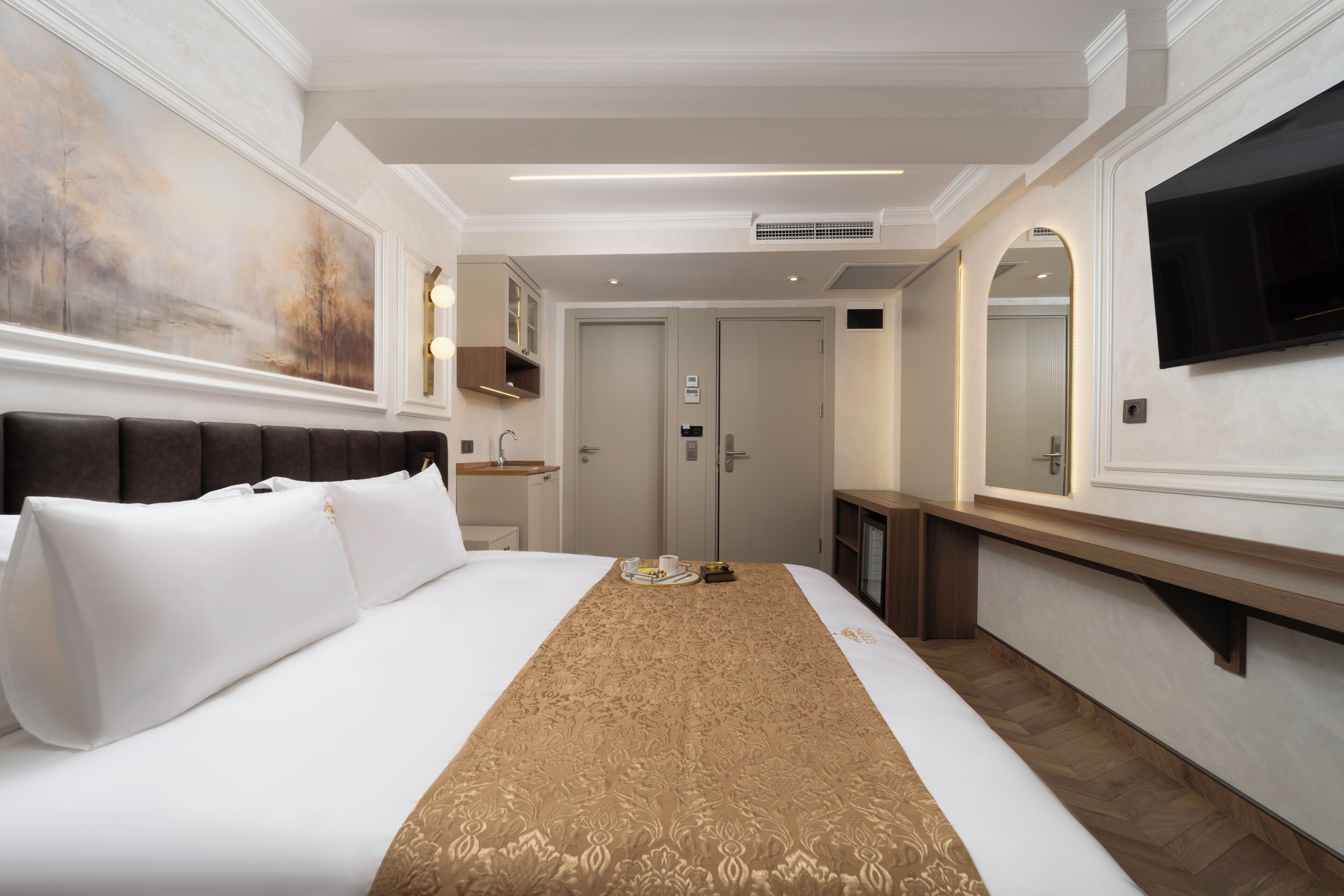 Ein Hotelzimmer mit einem großen Bett, einem an der Wand montierten Fernseher, einem Spiegel und einer Tür zu einem weiteren Raum.