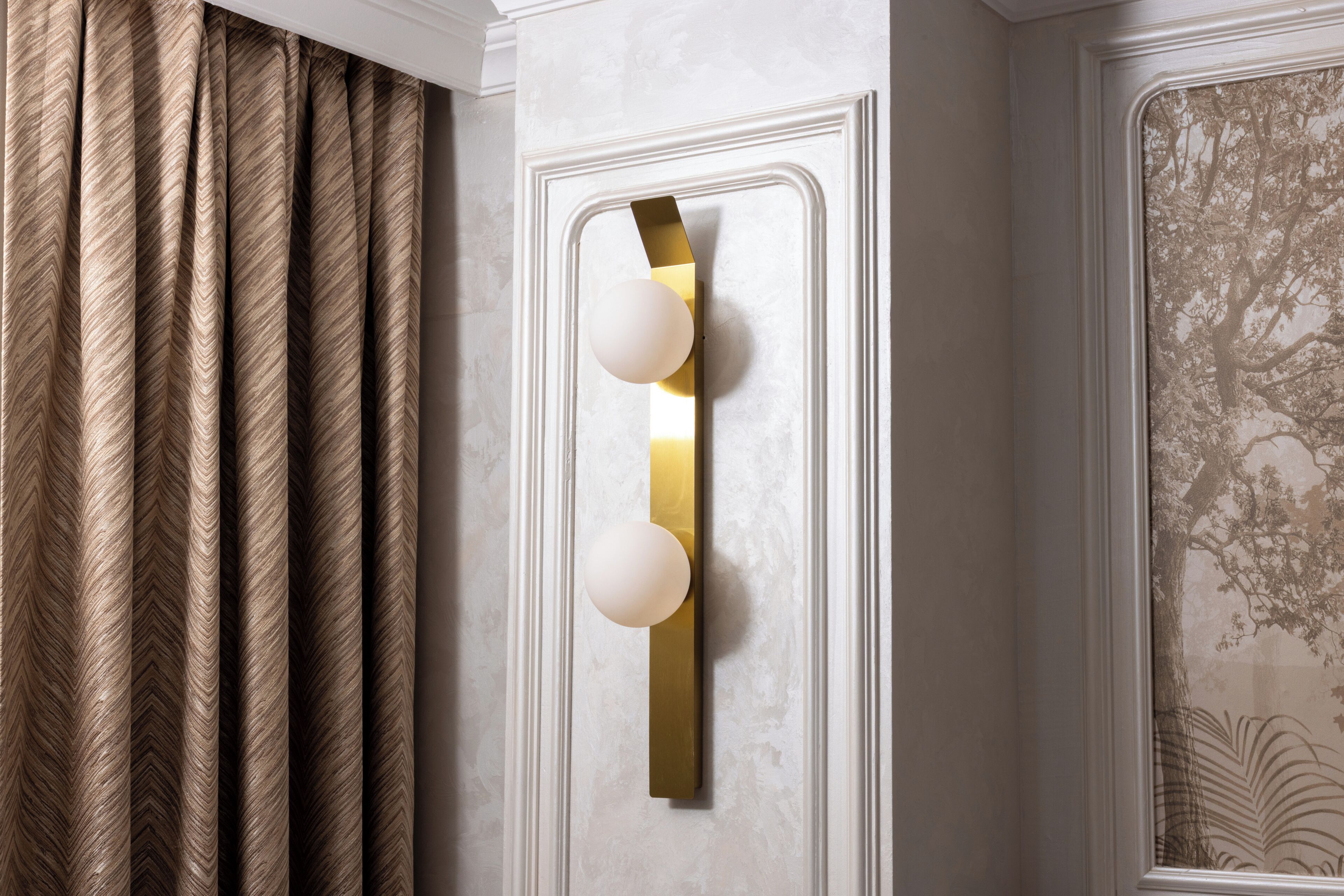 Un luminaire mural composé de trois sphères lumineuses, un rideau à motifs et un élément décoratif encadré fixé au mur.