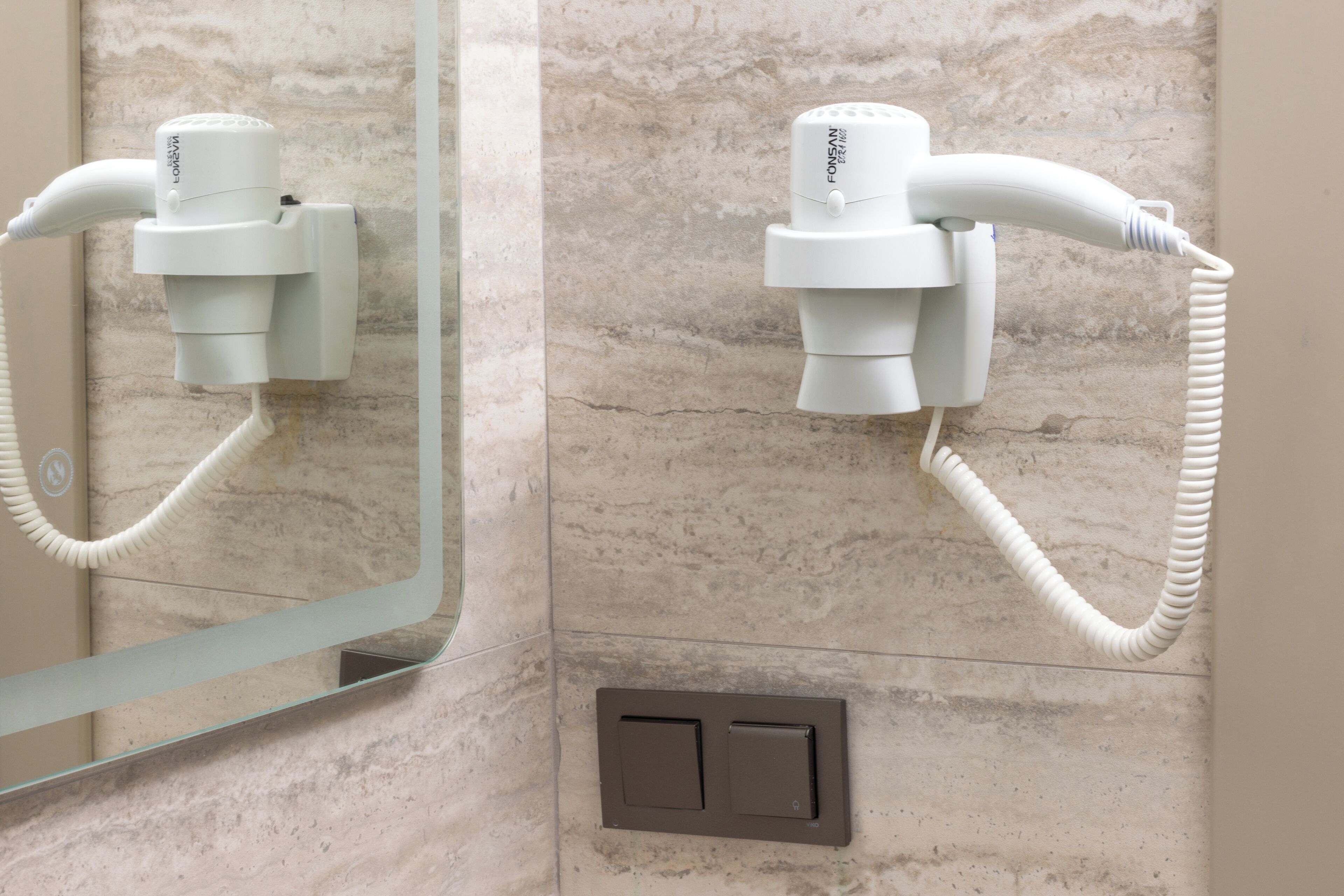 Une salle de bain équipée d’un sèche-cheveux fixé au mur, d’un miroir et d’un interrupteur.