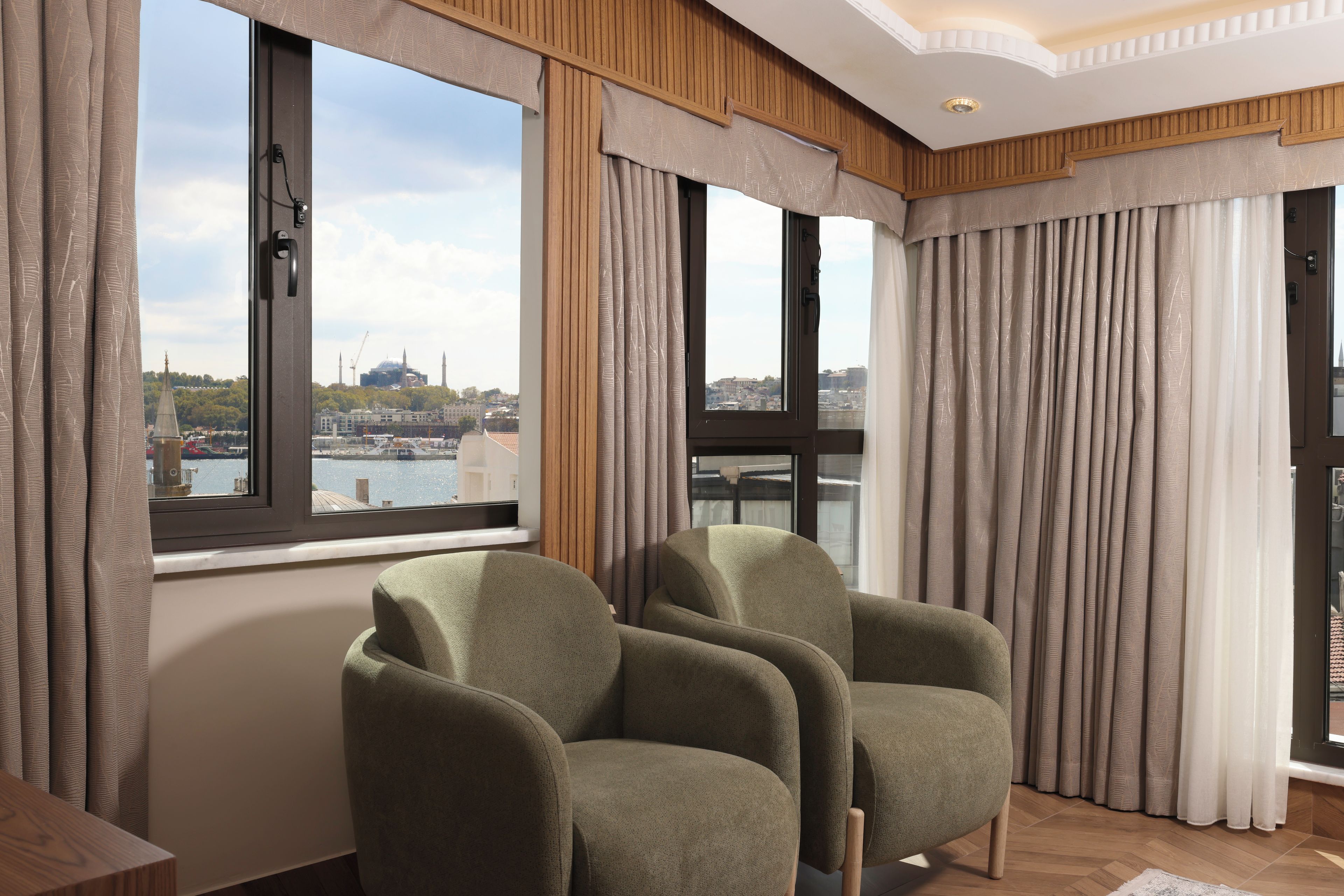 Ein modernes Zimmer mit einem großen Fenster, zwei grünen Sesseln und Blick auf eine Stadtlandschaft.
