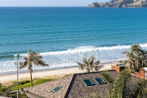 Blick auf einen Strand mit einem Haus, Palmen und blauem Himmel.