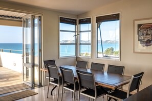 Ein Essbereich mit Tisch und Stühlen, große Fenster mit Meerblick und eine Tür zu einem Außenbalkon.