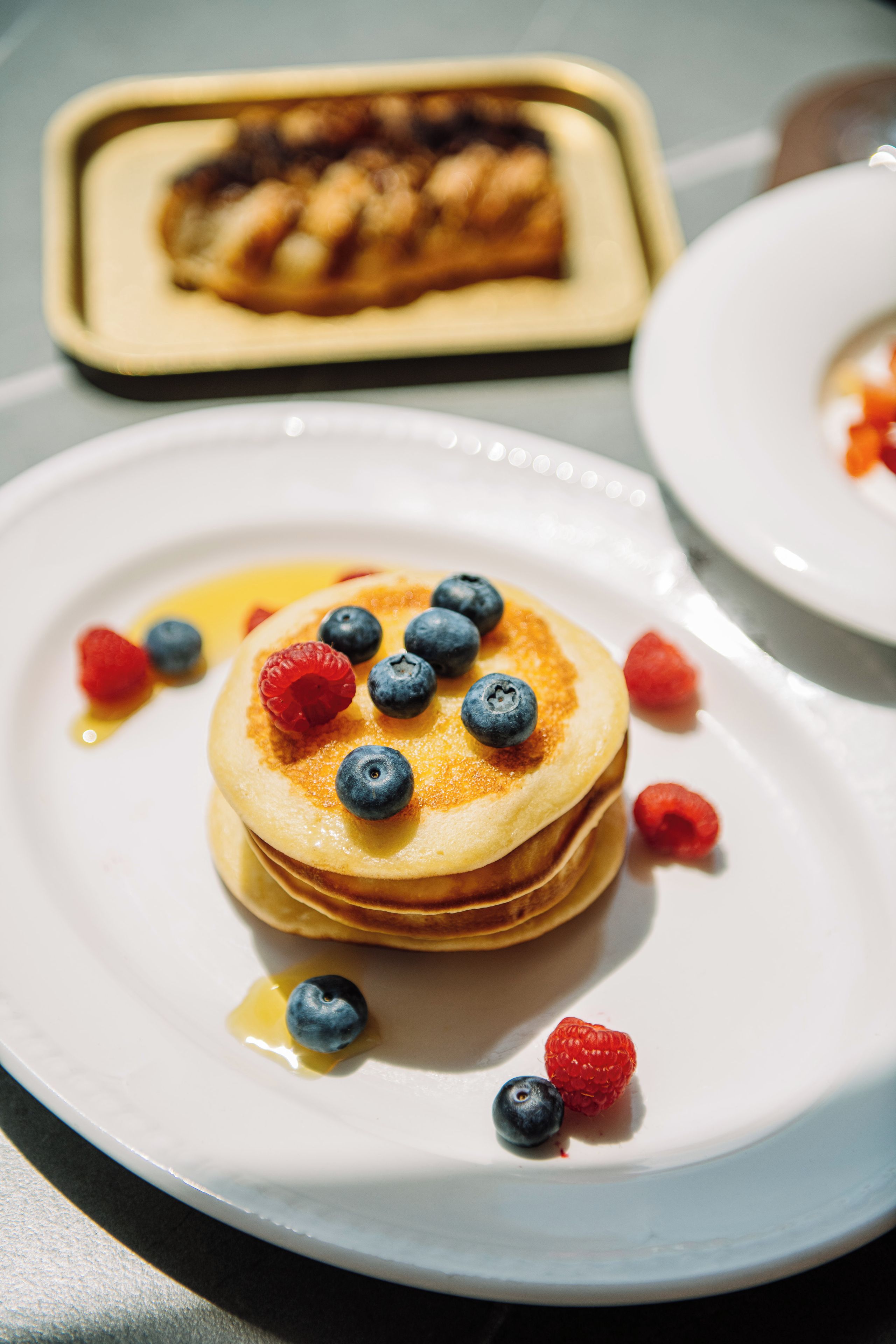 A stack of pancakes with blueberries and raspberries on a white plate.