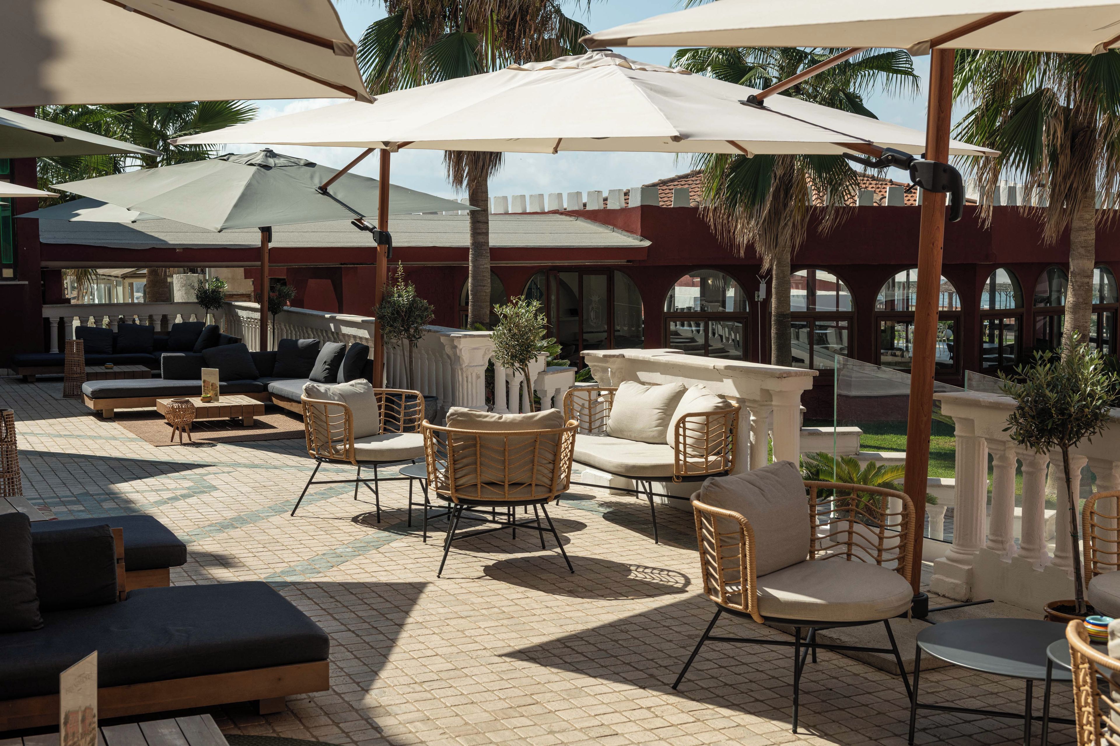 An outdoor seating area with wicker furniture, umbrellas, and a tiled floor.