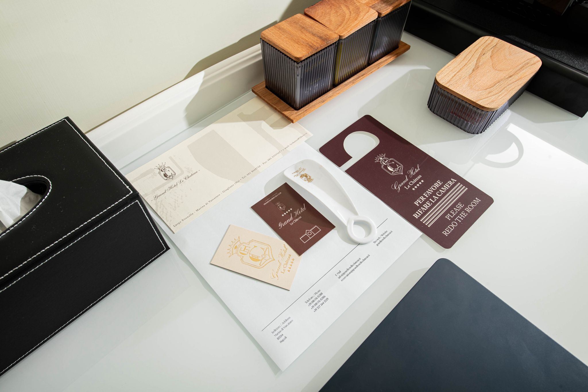 Une chambre d’hôtel équipée d’un bureau, d’une boîte à mouchoirs noire, d’un plateau en bois avec une boîte à mouchoirs, et d’un jeu de cartes comprenant une carte de bienvenue et une clé de chambre.