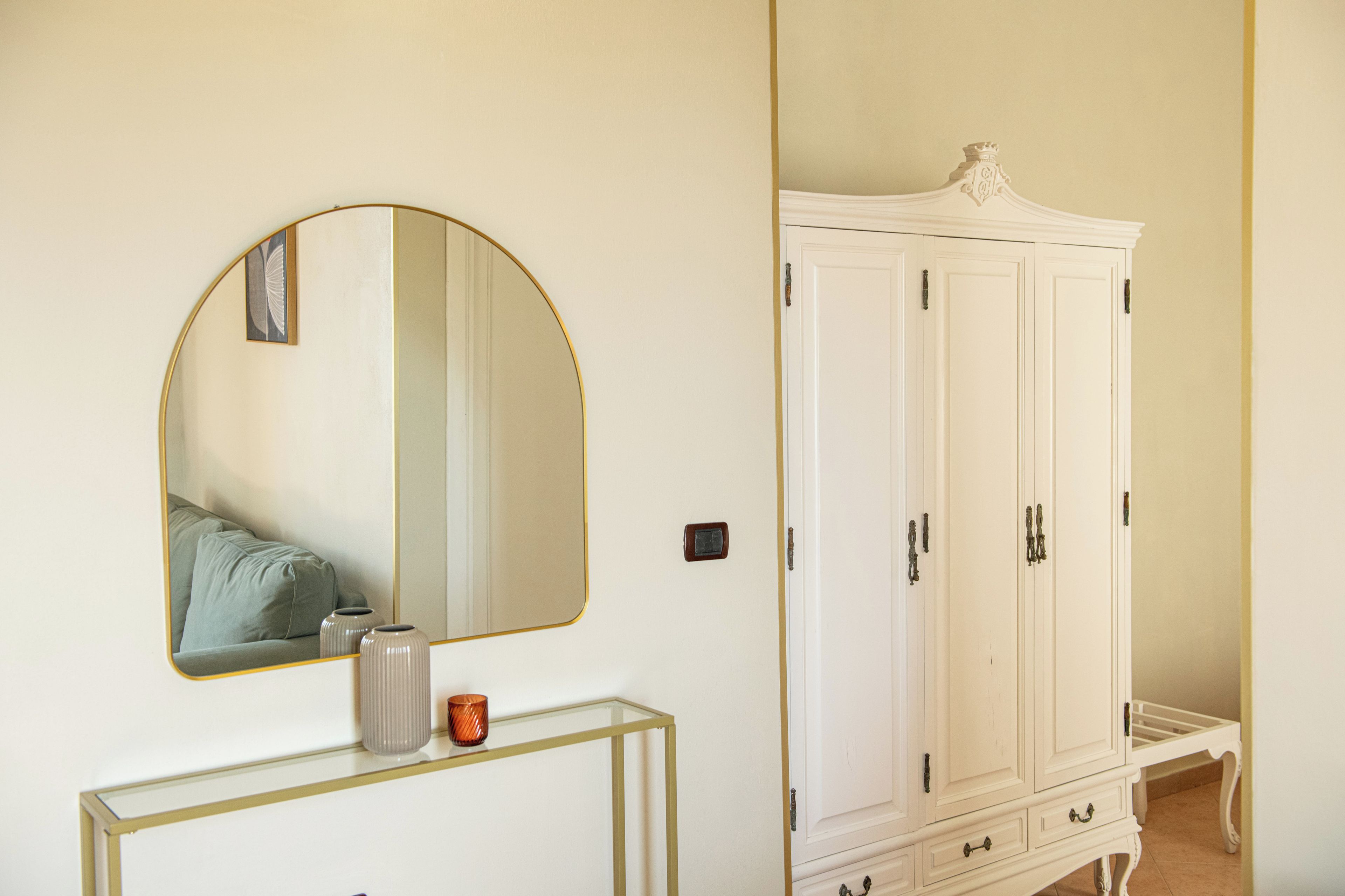 A room with a white wardrobe, a console table with a mirror, and a vase.