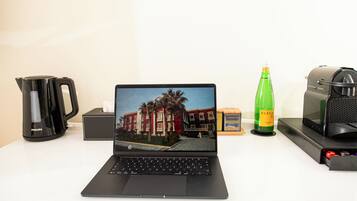 A laptop on a desk with a coffee maker, a bottle, and a speaker.