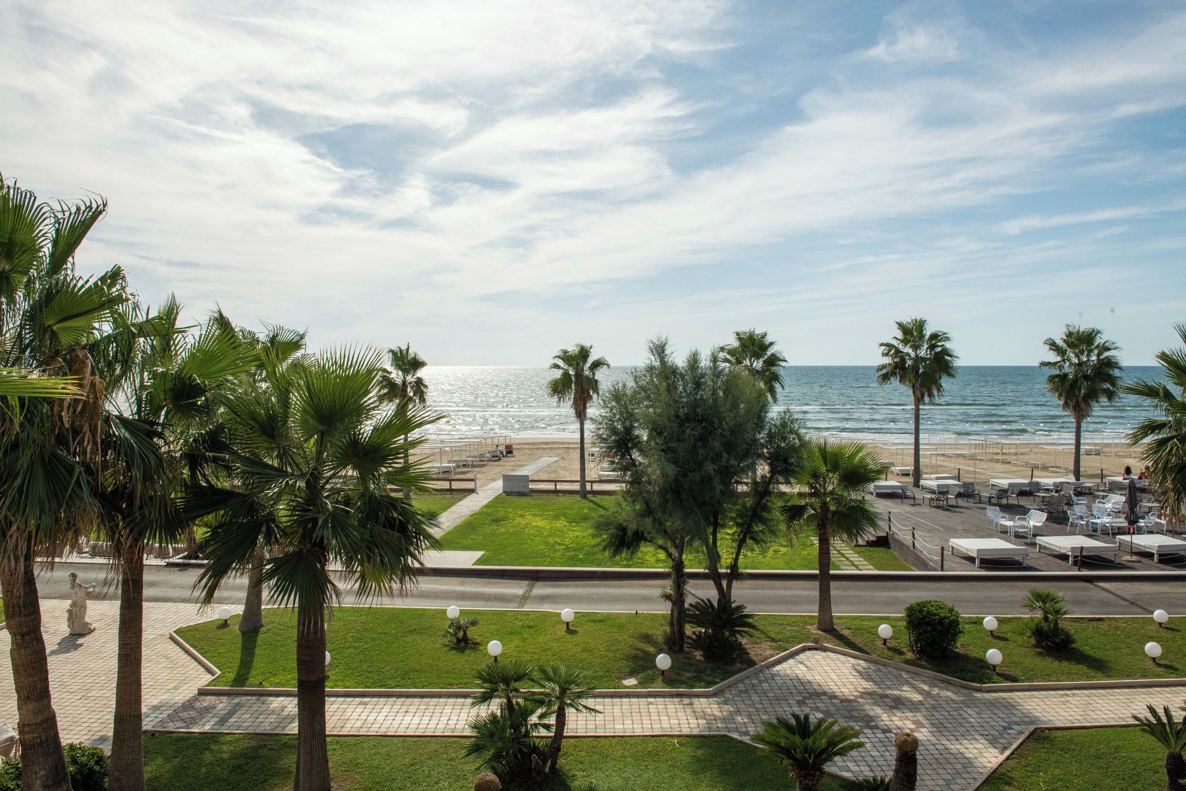 Un paseo marítimo frente a la playa con palmeras, una pasarela y sillas para tomar el sol.