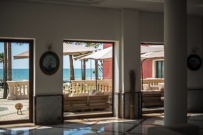 Vestíbulo de hotel con vista al océano, asientos exteriores y una palmera.