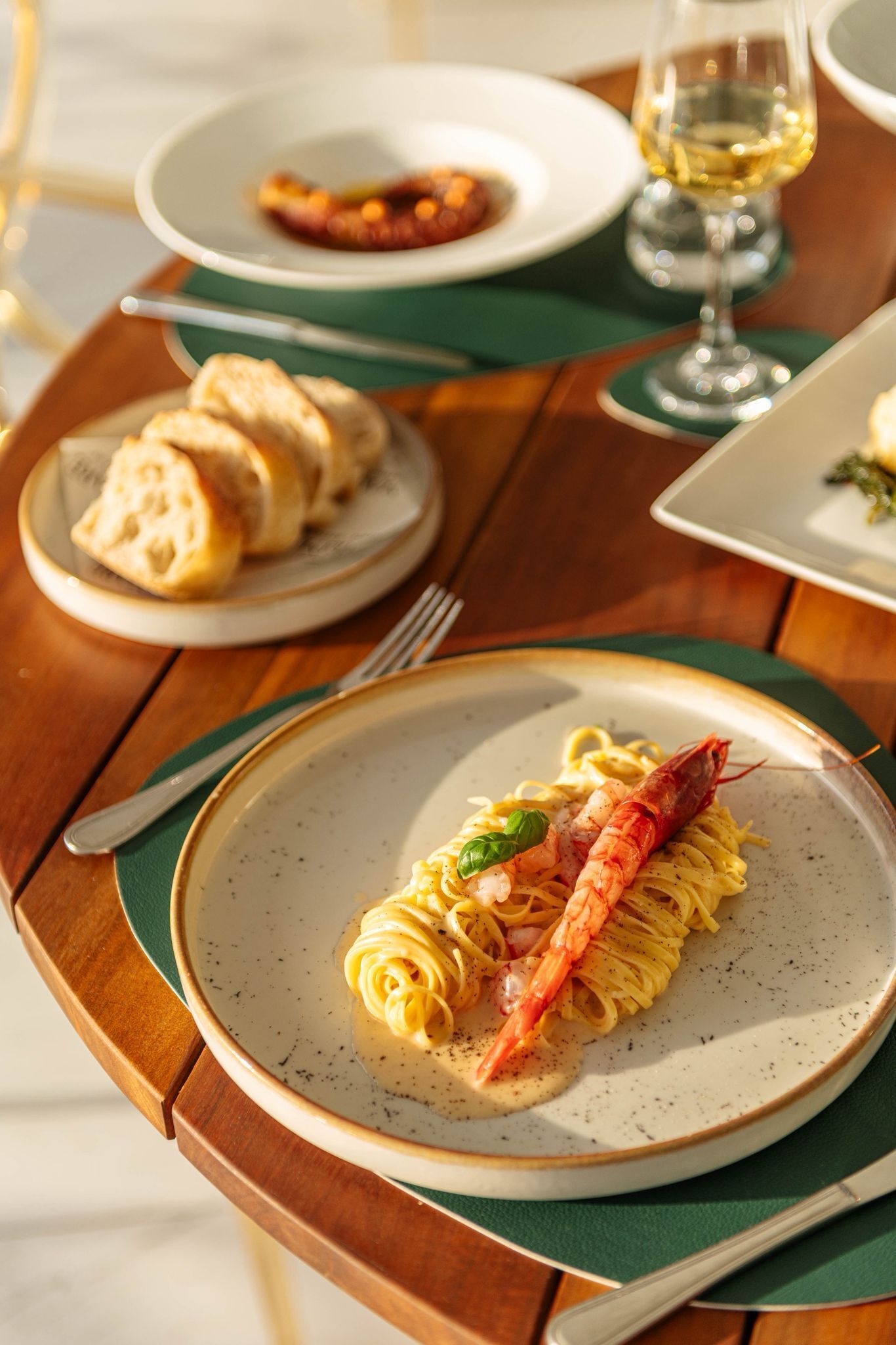 A dining table with plates of pasta and bread, a glass of wine, and cutlery.