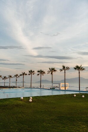 A pool area with palm trees, a lounge chair, and a clear view of the ocean. - Grand Hotel Le Château (Giugliano in Campania)