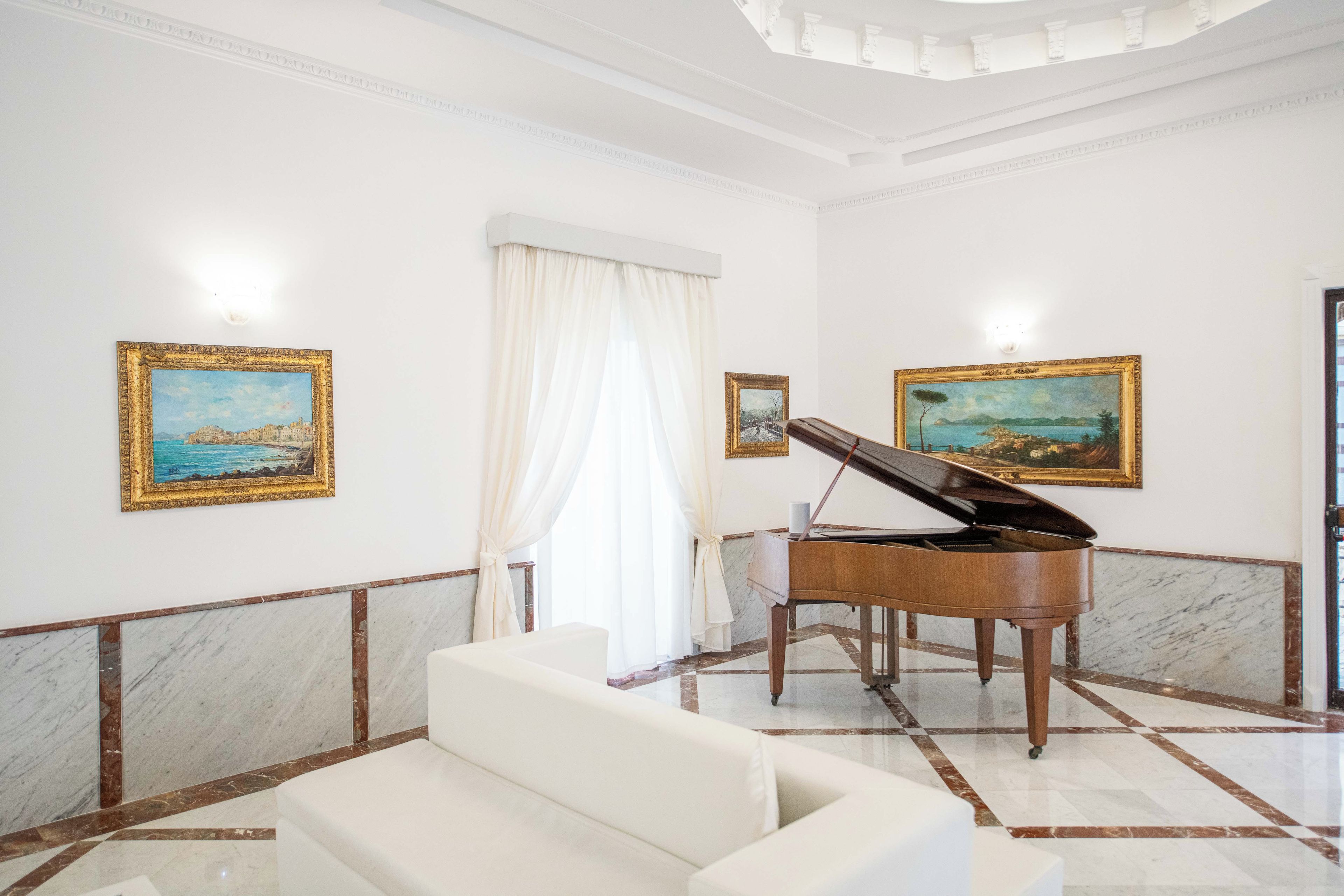 A grand room with a grand piano, marble flooring, and two framed paintings on the walls.