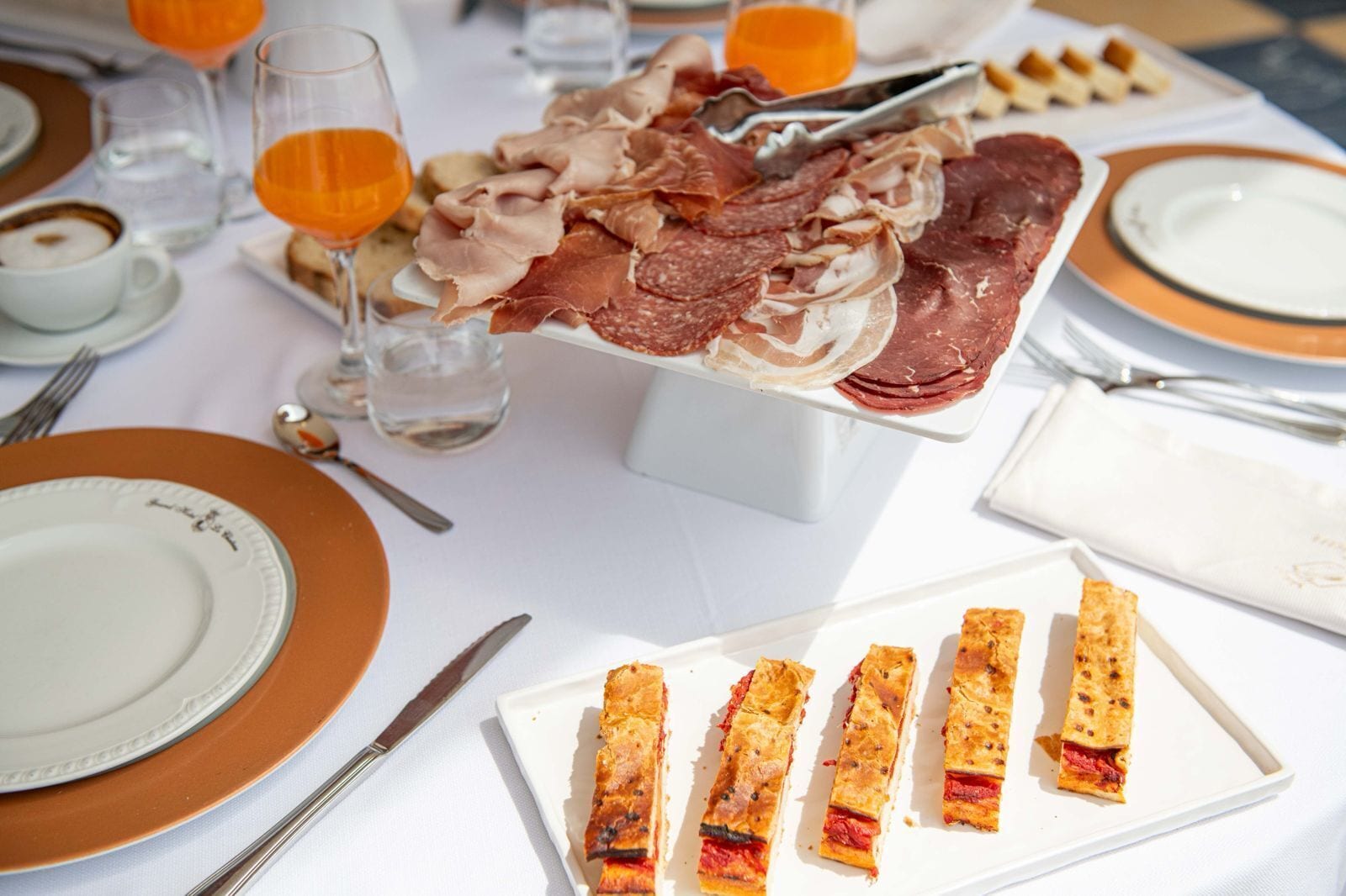 Une table dressée avec des assiettes, des couverts et une variété de viandes et de pâtisseries.
