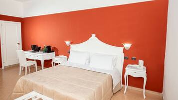 Une chambre d’hôtel avec un lit, un bureau blanc, une chaise, des tables de chevet et un mur d’accent rouge.