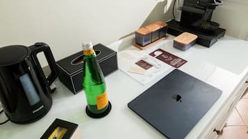 A hotel room counter with a coffee maker, a bottle of water, a laptop, and some boxes.