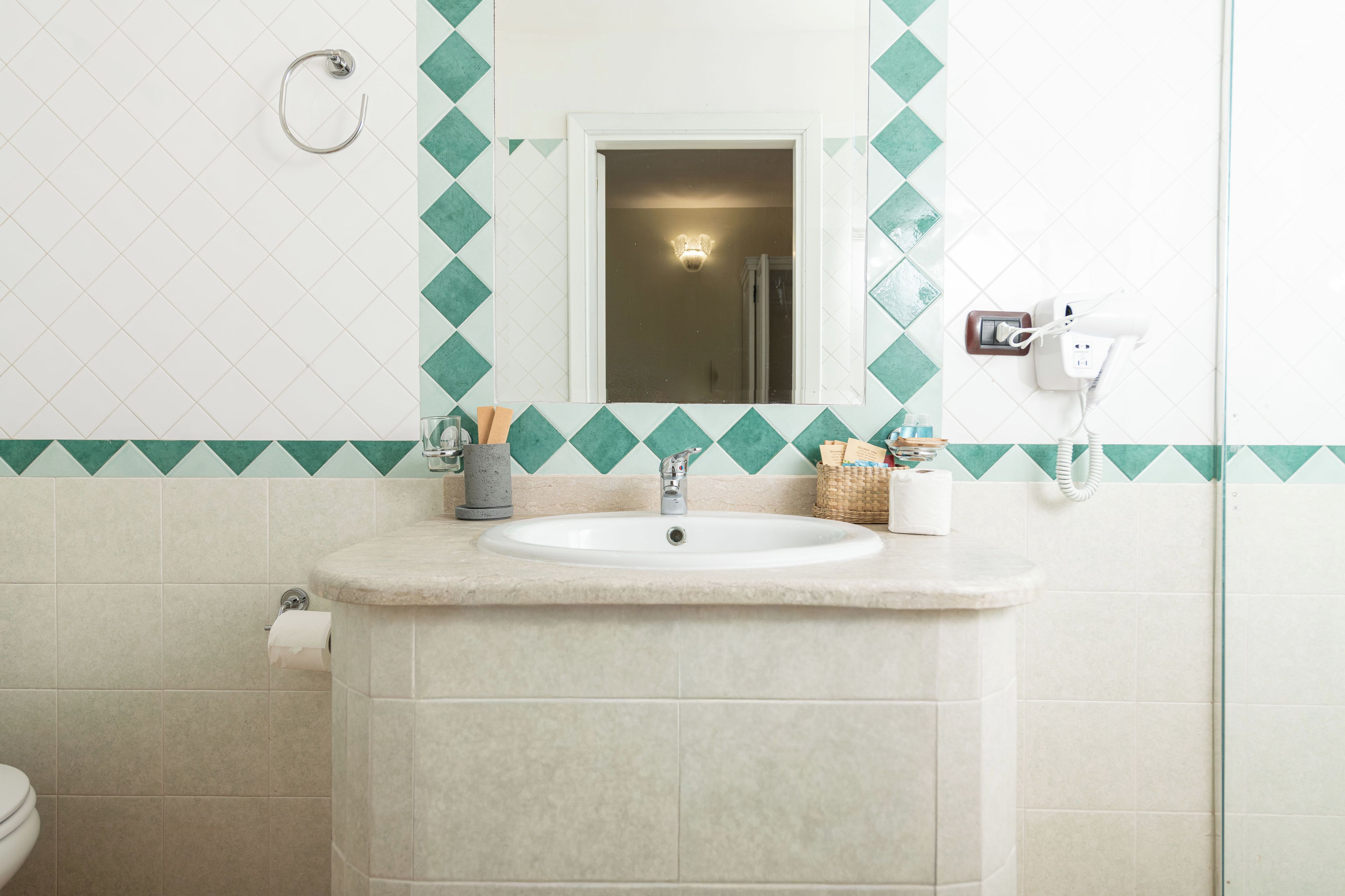 A bathroom with a sink, mirror, and a towel dispenser.