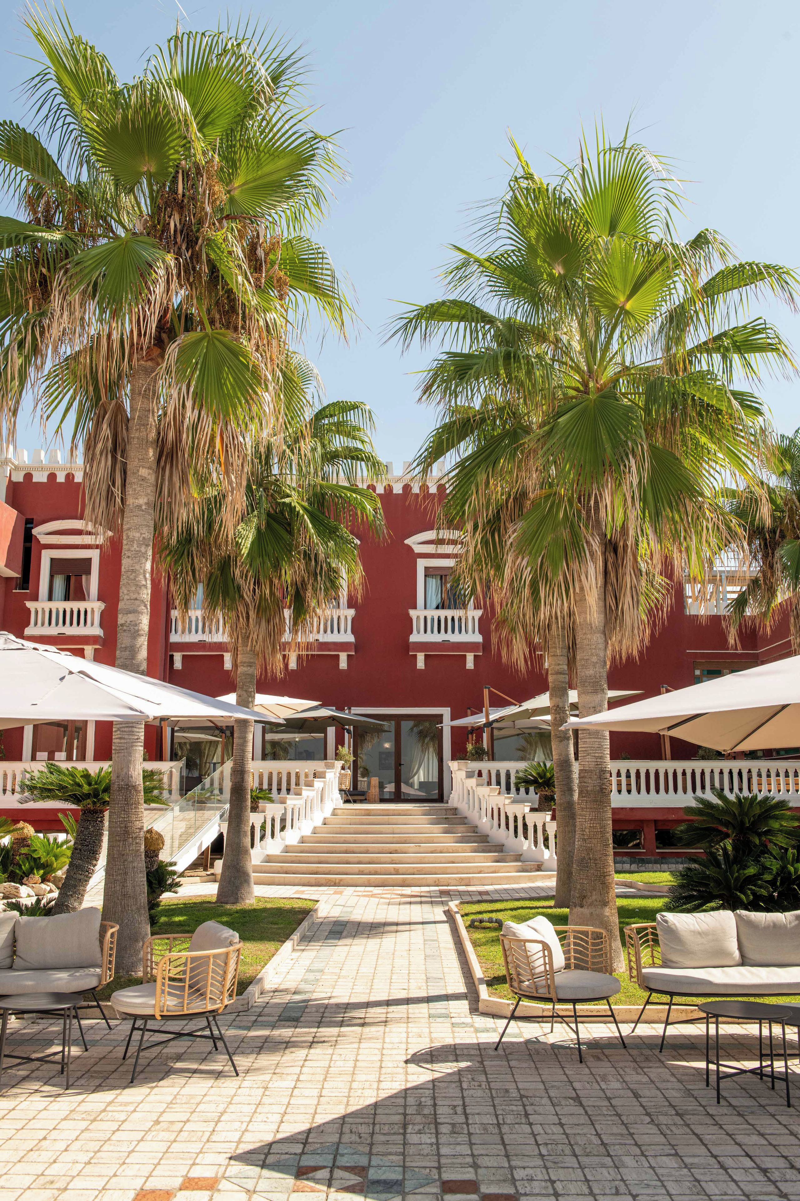 A courtyard with palm trees, outdoor seating, and a red building with balconies.