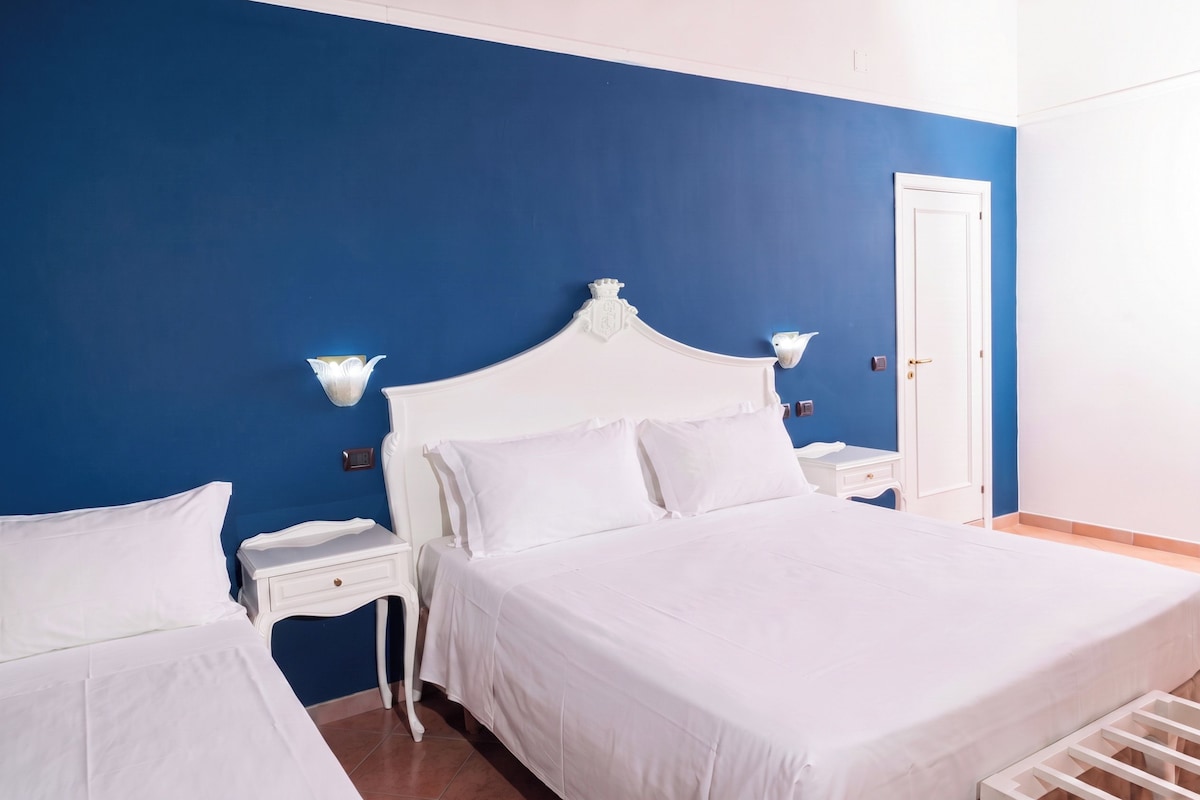 A hotel room with a large bed, a bedside table, a nightstand, a wall-mounted light, and a door.