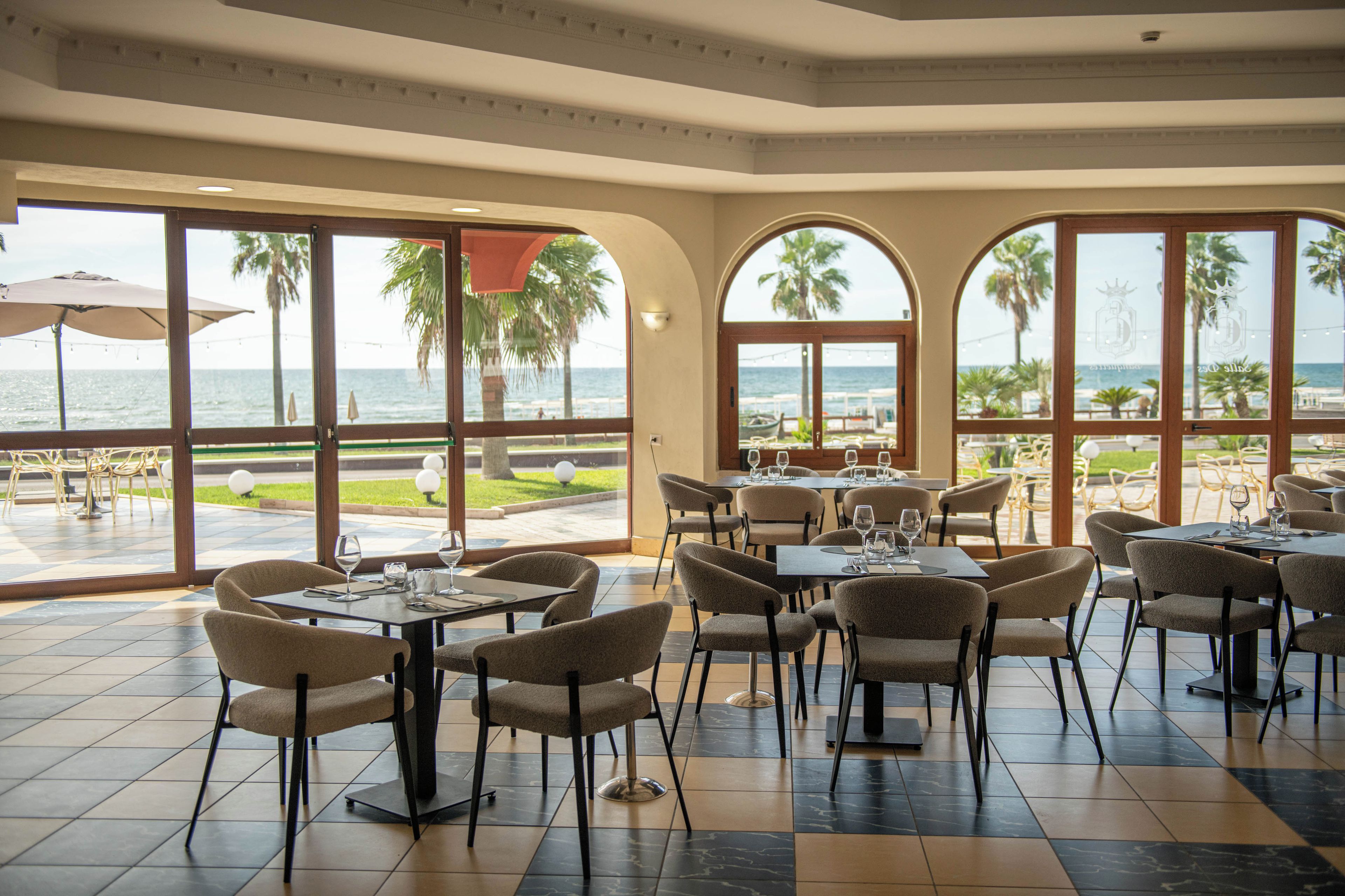 A restaurant with outdoor seating overlooking the sea, featuring tables and chairs arranged for dining.