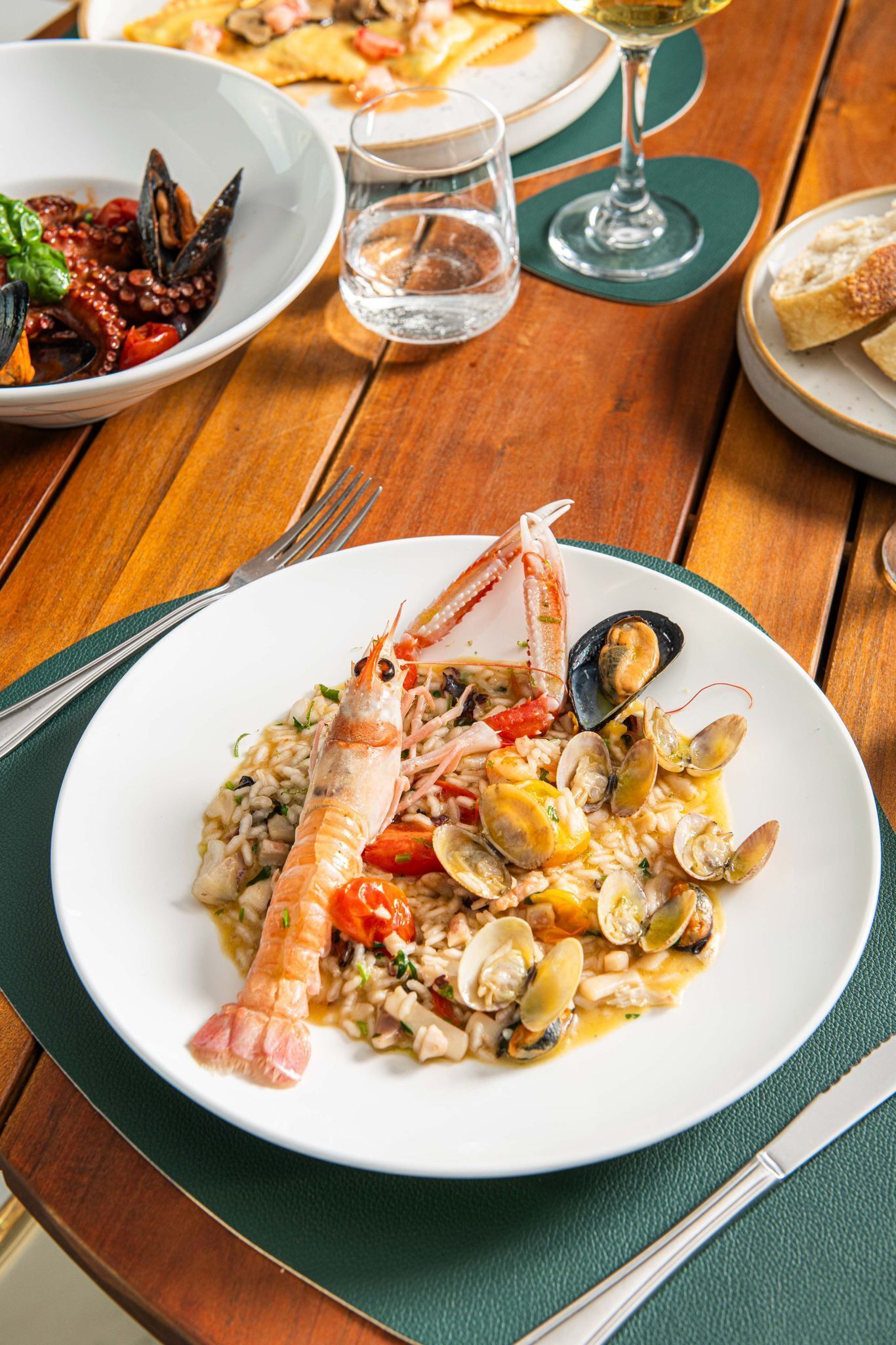 A seafood dish on a white plate with a green placemat, accompanied by a fork and knife on a wooden table.