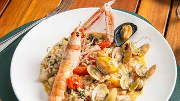A seafood dish on a white plate with a green placemat, accompanied by a fork and knife on a wooden table.