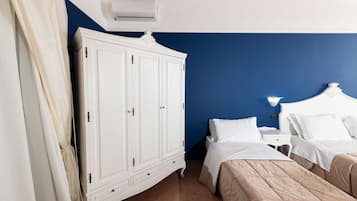 A bedroom with a white wardrobe, two beds, a nightstand, and a wall-mounted air conditioner.