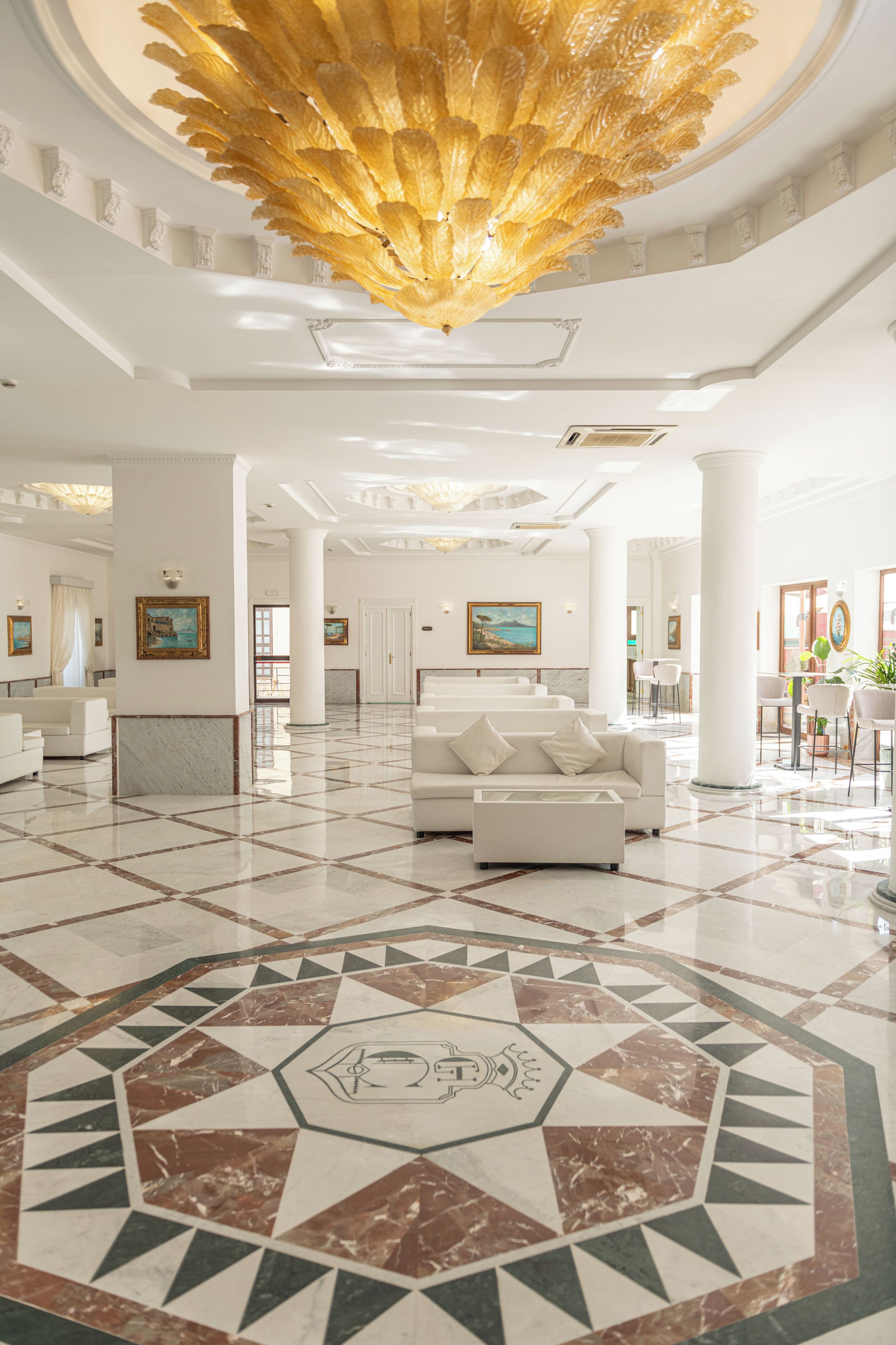 A spacious lobby with a geometric patterned floor, a central seating area with sofas, and a large decorative ceiling feature.