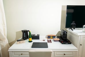 A neatly arranged hotel desk with a laptop, a bottle of Electa sparkling water, a tea box, a tissue box, a coffee maker, and a small lantern. - Grand Hotel Le Château (Giugliano in Campania)