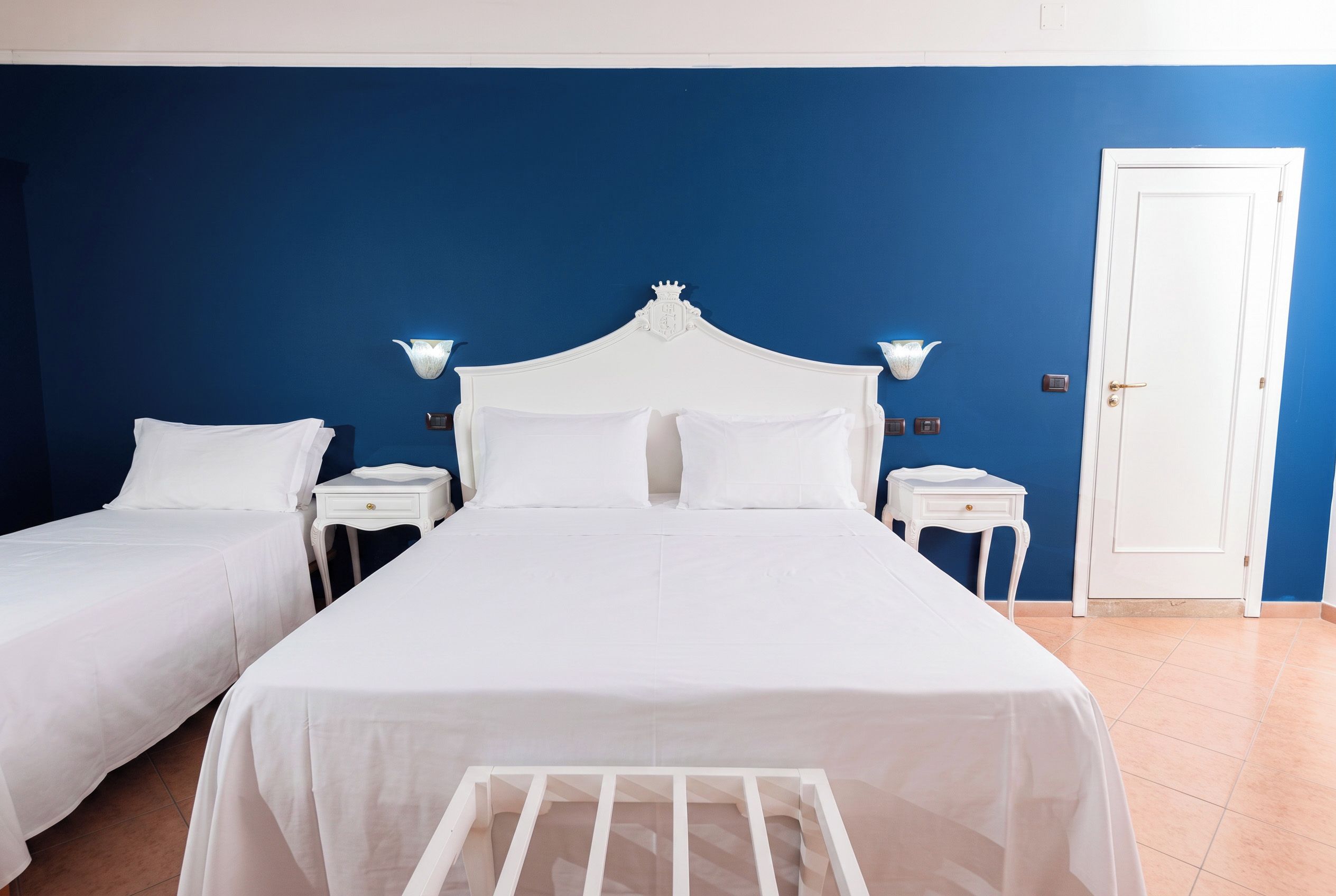 Una habitación de hotel con una cama grande, dos mesitas de noche, un armario y una puerta.