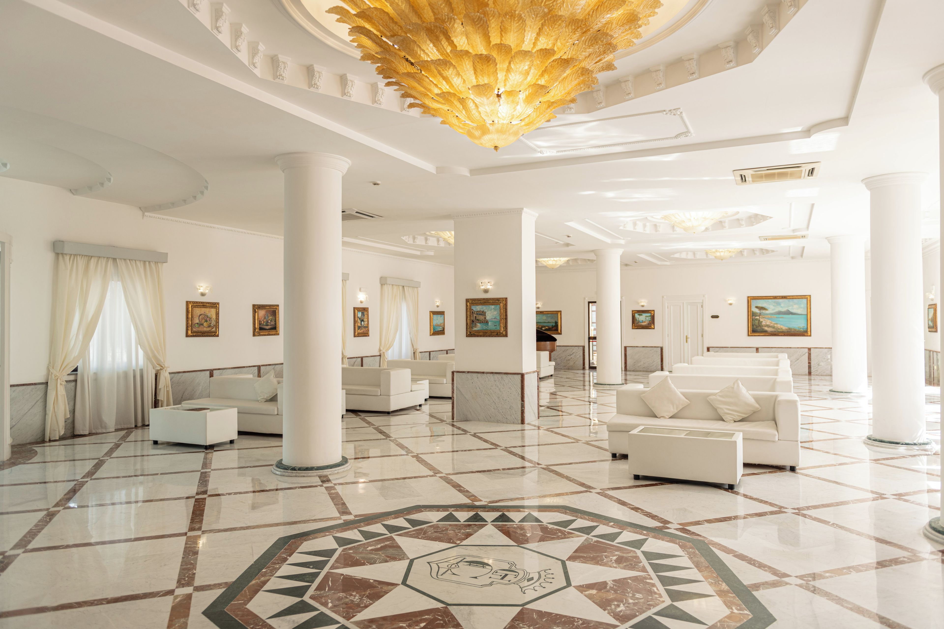 A spacious lobby with white columns, a patterned floor, and a large chandelier.