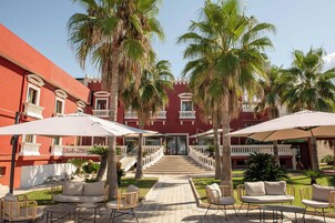 Un patio con mobiliario exterior, palmeras y un edificio con balcones.