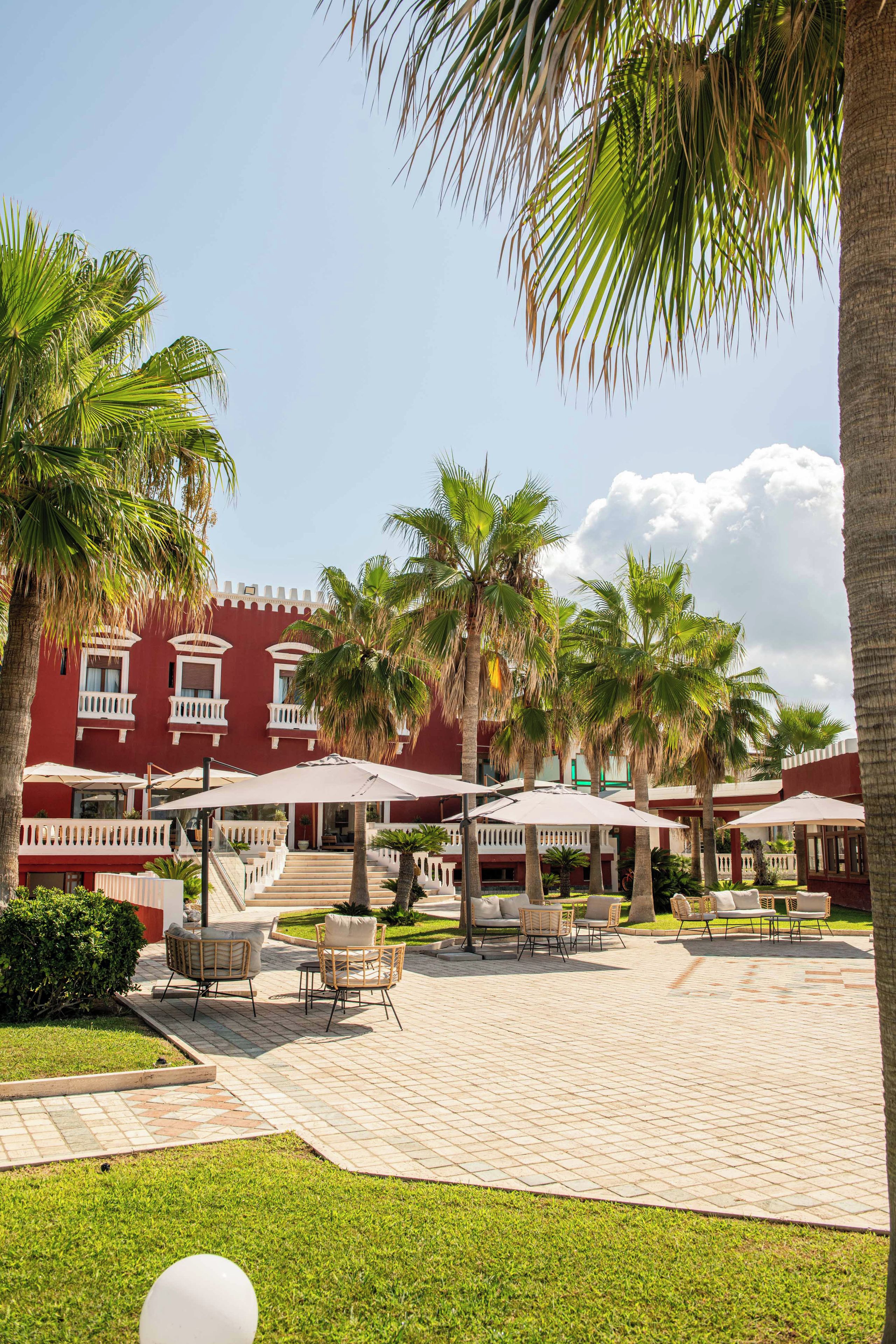A courtyard with palm trees, outdoor seating, and a red building with balconies.