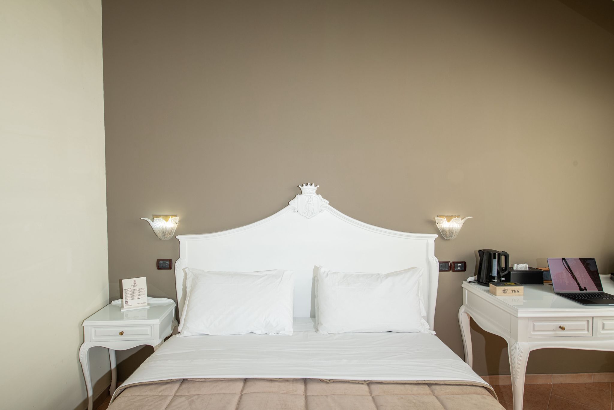 A neatly arranged hotel room with a bed, bedside tables, a desk, and a lamp.