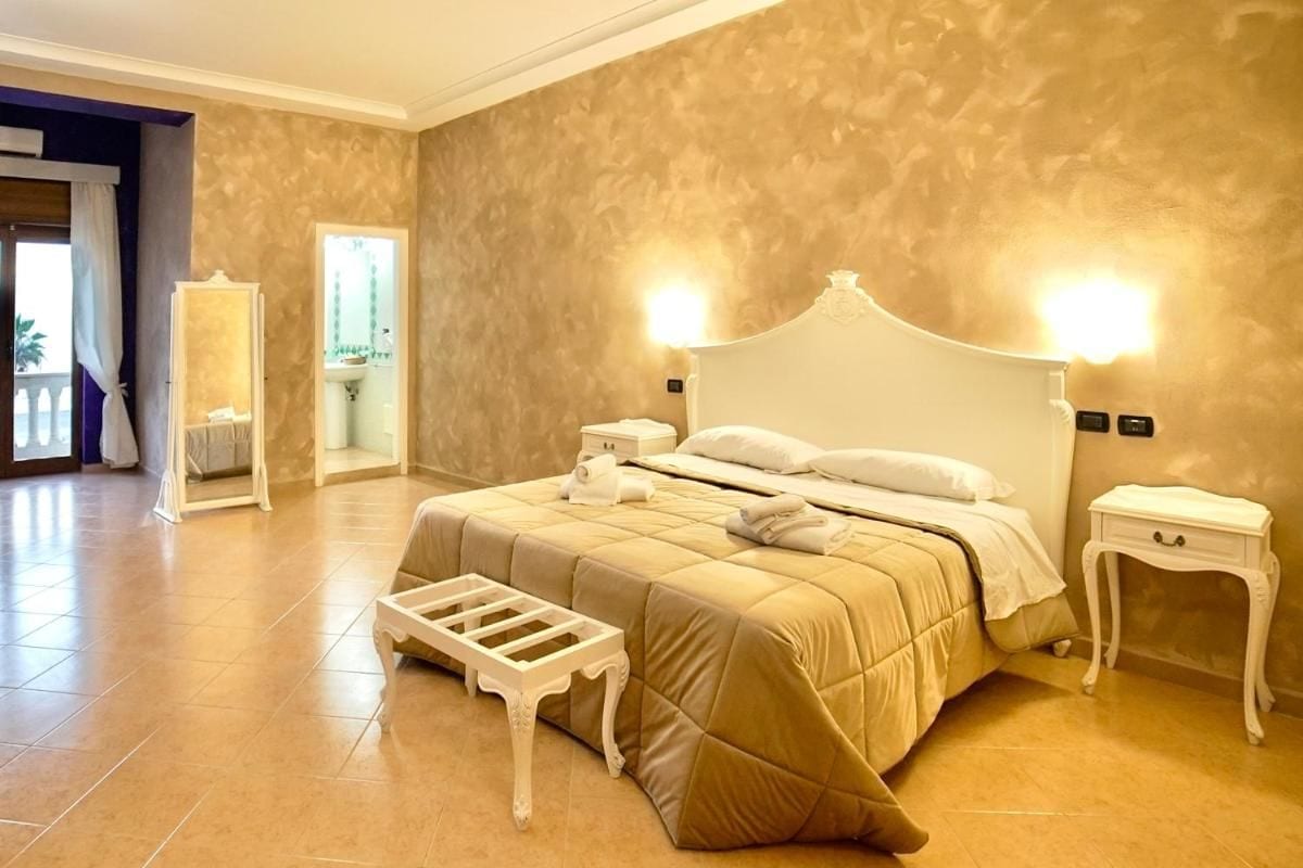 A hotel room with a large bed, bedside tables, a mirror, and a view of the outside.