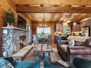 Ein gemütliches Blockhaus mit Kamin aus Stein, Esstisch aus Holz, Ledersofa und Küchenzeile.