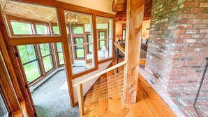 Una escalera de madera con barandilla de metal que lleva a una habitación con ventanas amplias y pared de ladrillo.