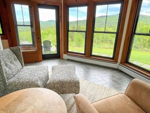 Ein Eckzimmer mit großem Fenster, einer Tür und Blick auf eine grüne Landschaft.
